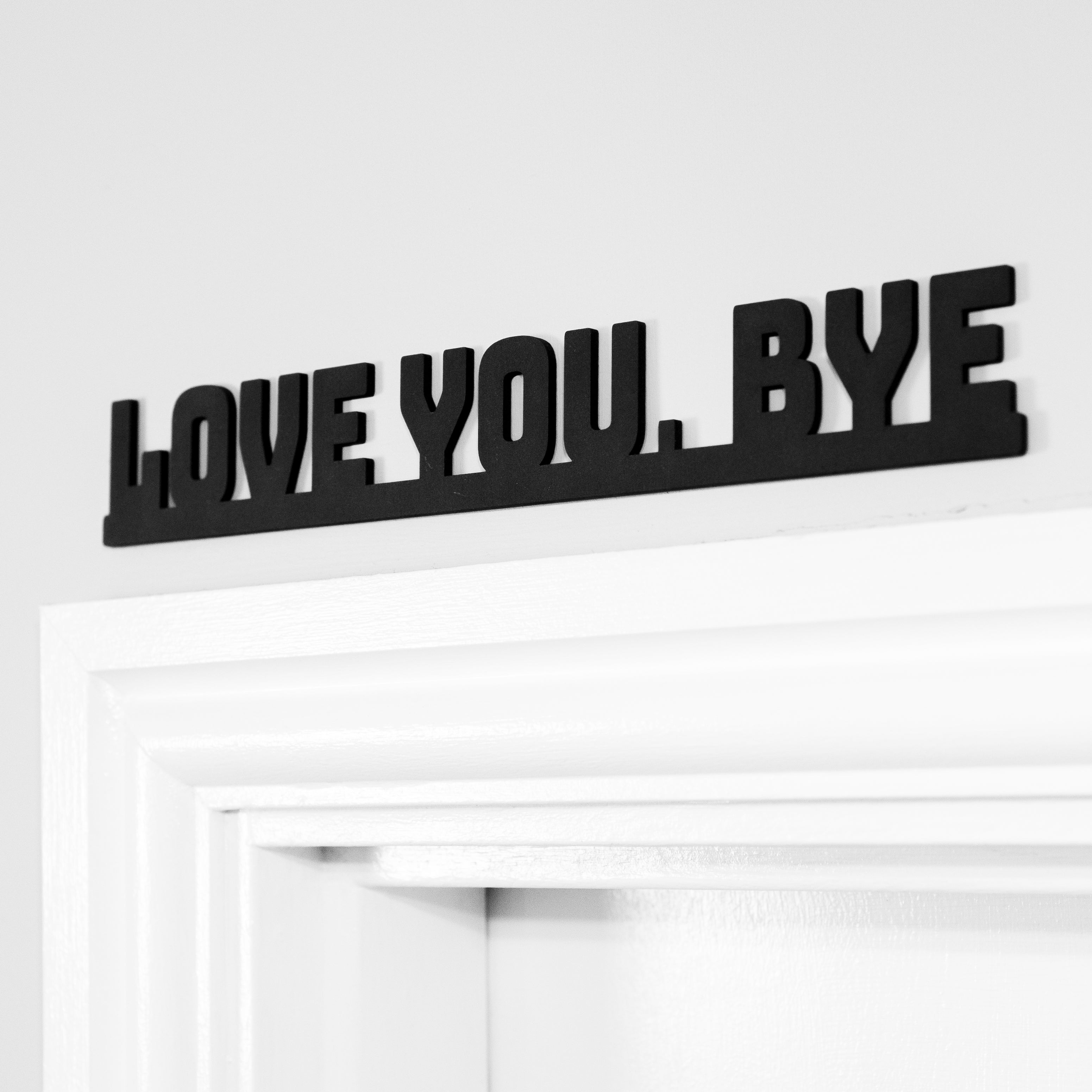 A black MDF door sign with the text 'love you bye' in white letters, mounted on a white door.