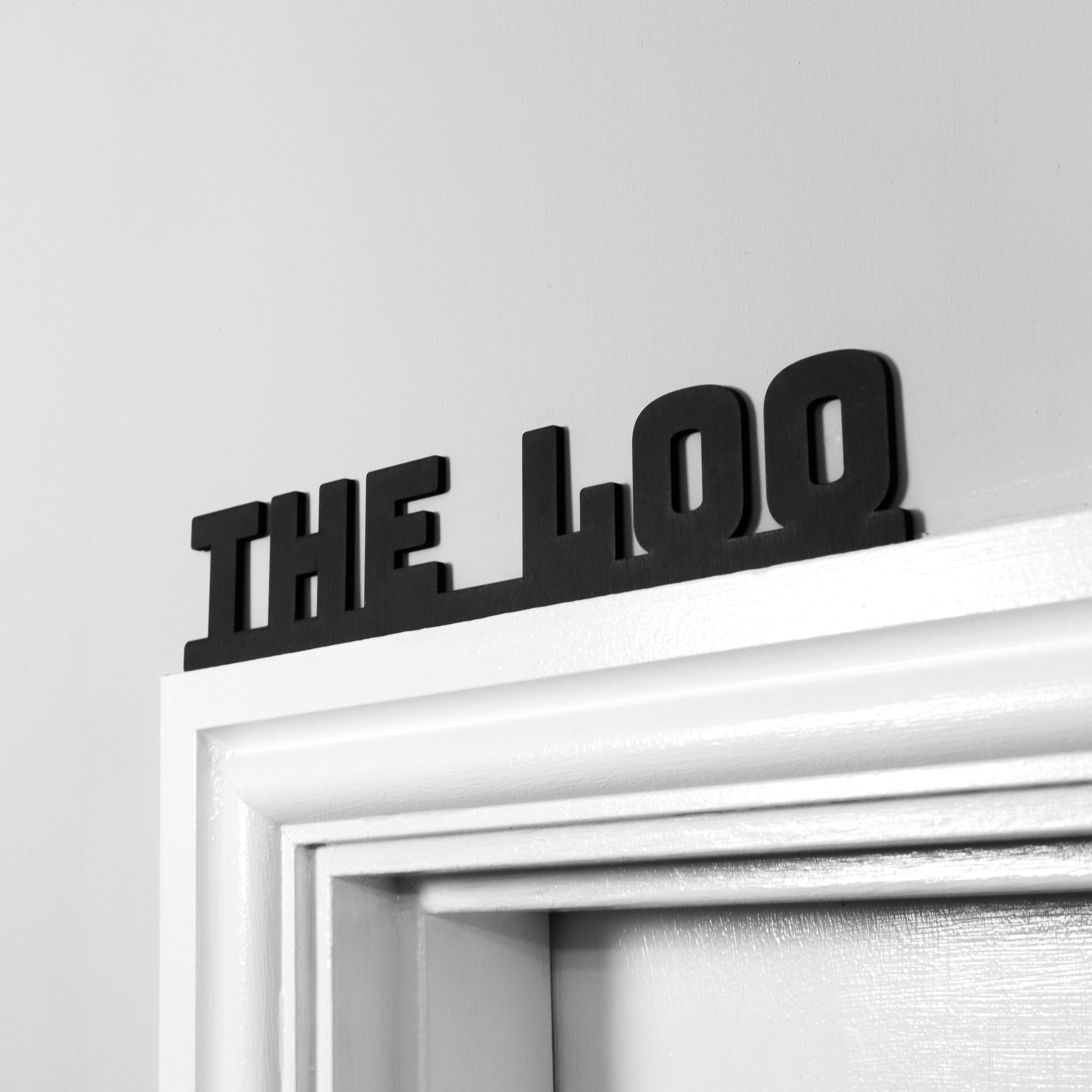 A black text 'the loo' wall sign mounted on a white door frame.