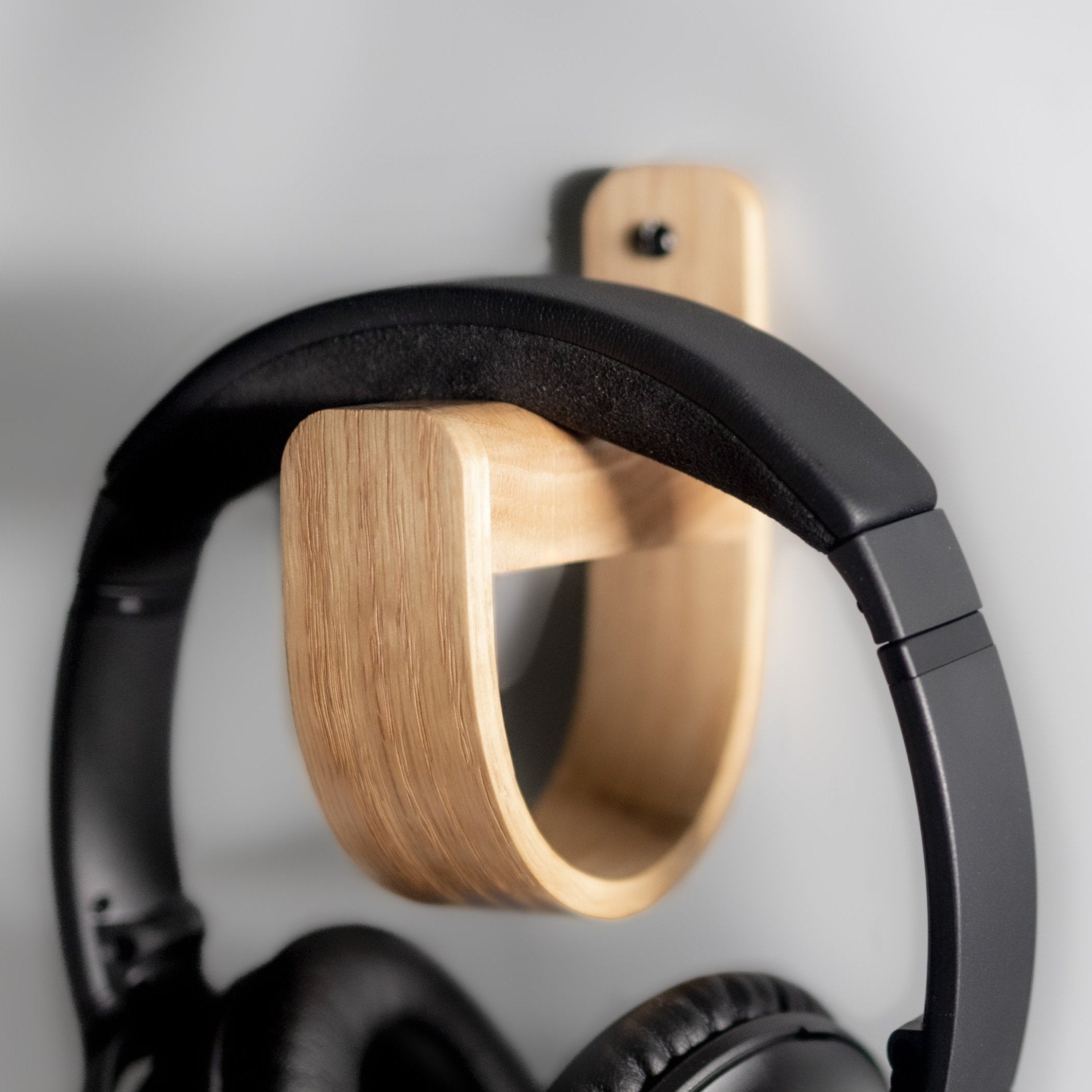 Wall-mounted headphone holder made of oak wood, with a pair of headphones hanging on it.